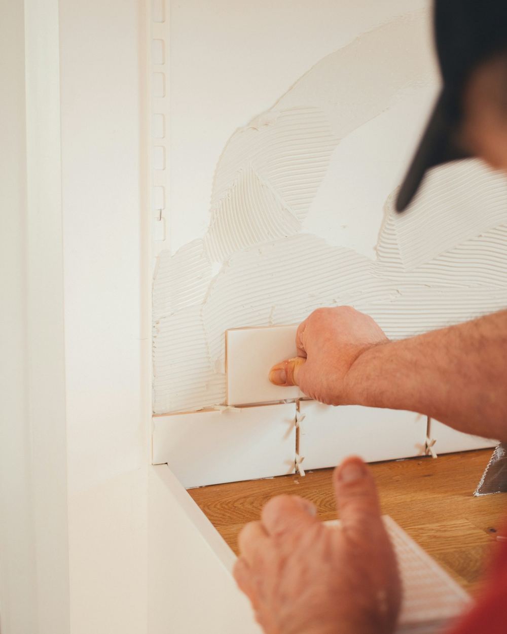 Tile installer setting a ceramic wall tile by hand and checking the seam