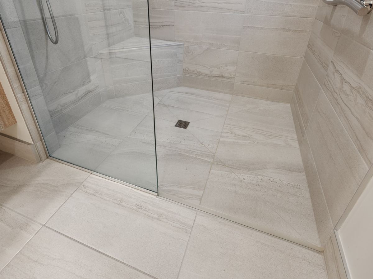 Large format porcelain floor tile installed in a bright bathroom with a glass shower panel