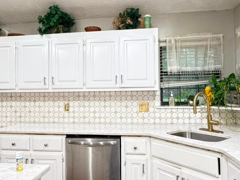 White penny round mosaic tile backsplash installed in a kitchen with white cabinets and a quartz counter